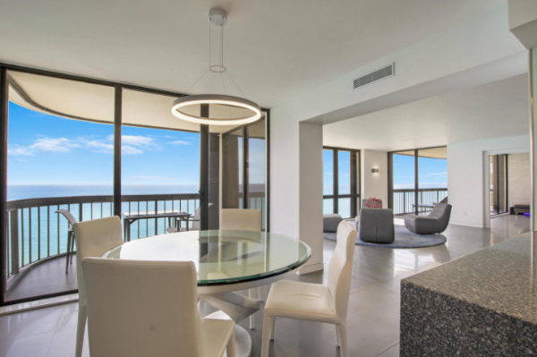 Dining area on the foreground and living room in the background of a Singer Island condo with floor to ceiling windows giving way to an ocean view